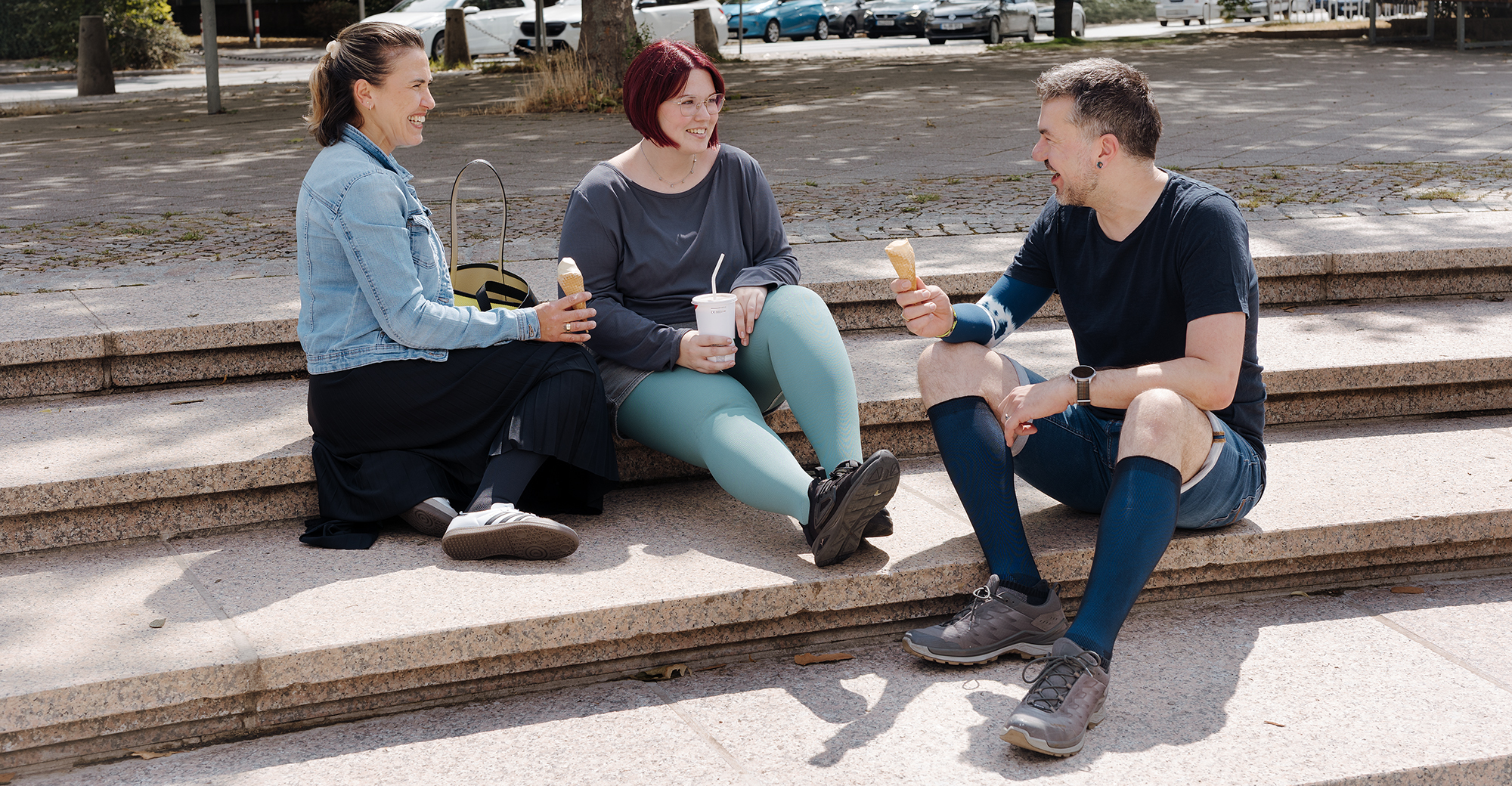 Auf dem Bild sieht man zwei Frauen und einen Mann, die sich unterhalten, zusammen lachen und ein Eis essen. Alle tragen Kompressionsstrümpfe in verschiedenen Ausführungen.