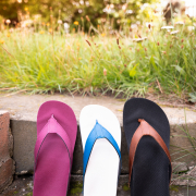 Auf dem Foto sieht man drei verschiedenfarbige Flip Flops, die auf einer Steintreppe angelehnt, an die zweite Stufe von oben stehen. Im Hintergrund sieht man Gras und den Ansatz von Büschen in der Unschärfe.